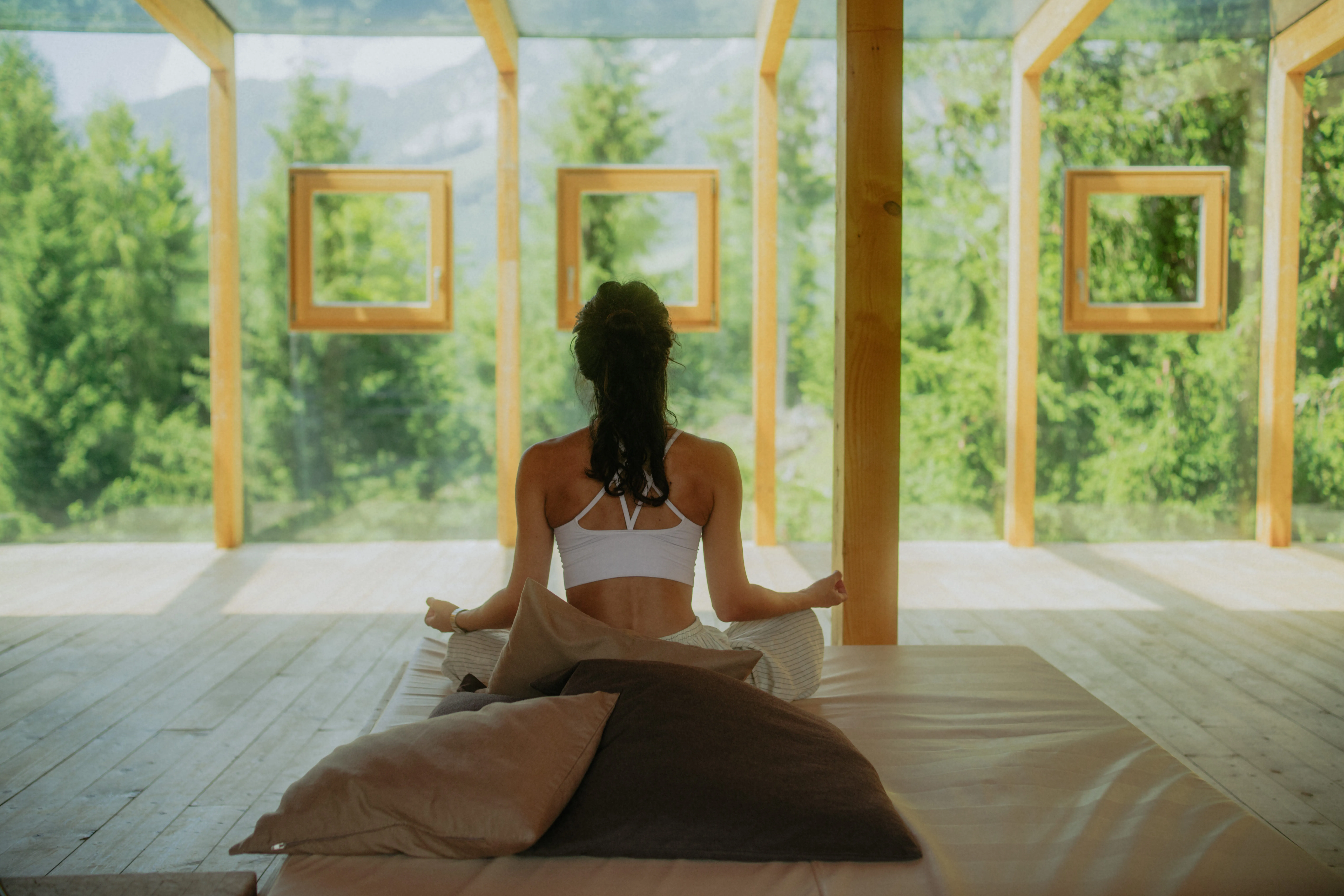 Frau in Yoga-Pose im Innenraum mit großen Fenstern und Blick auf Bäume