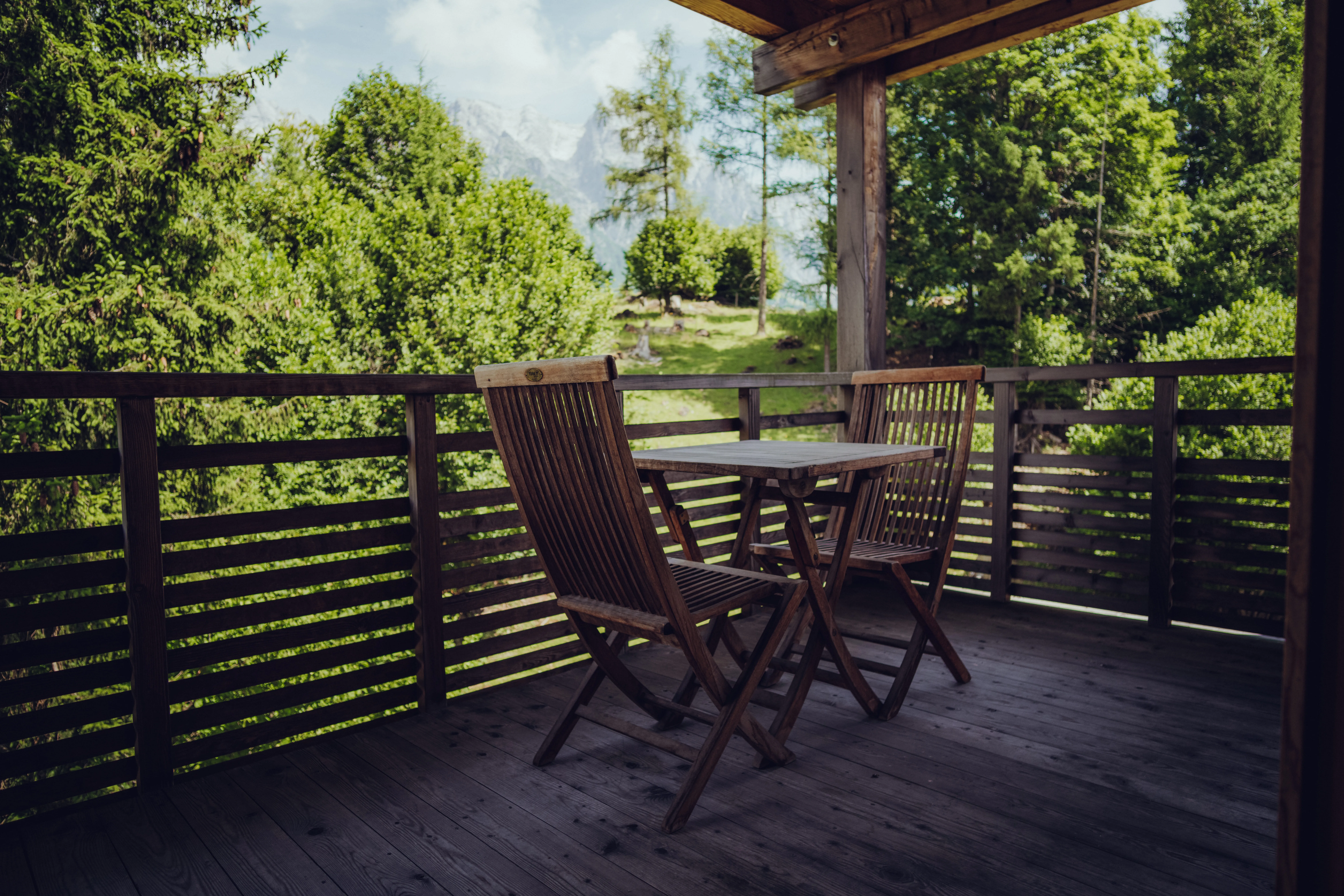 Balkon mit Holzstühlen und Tisch, Blick auf grüne Bäume und Berge