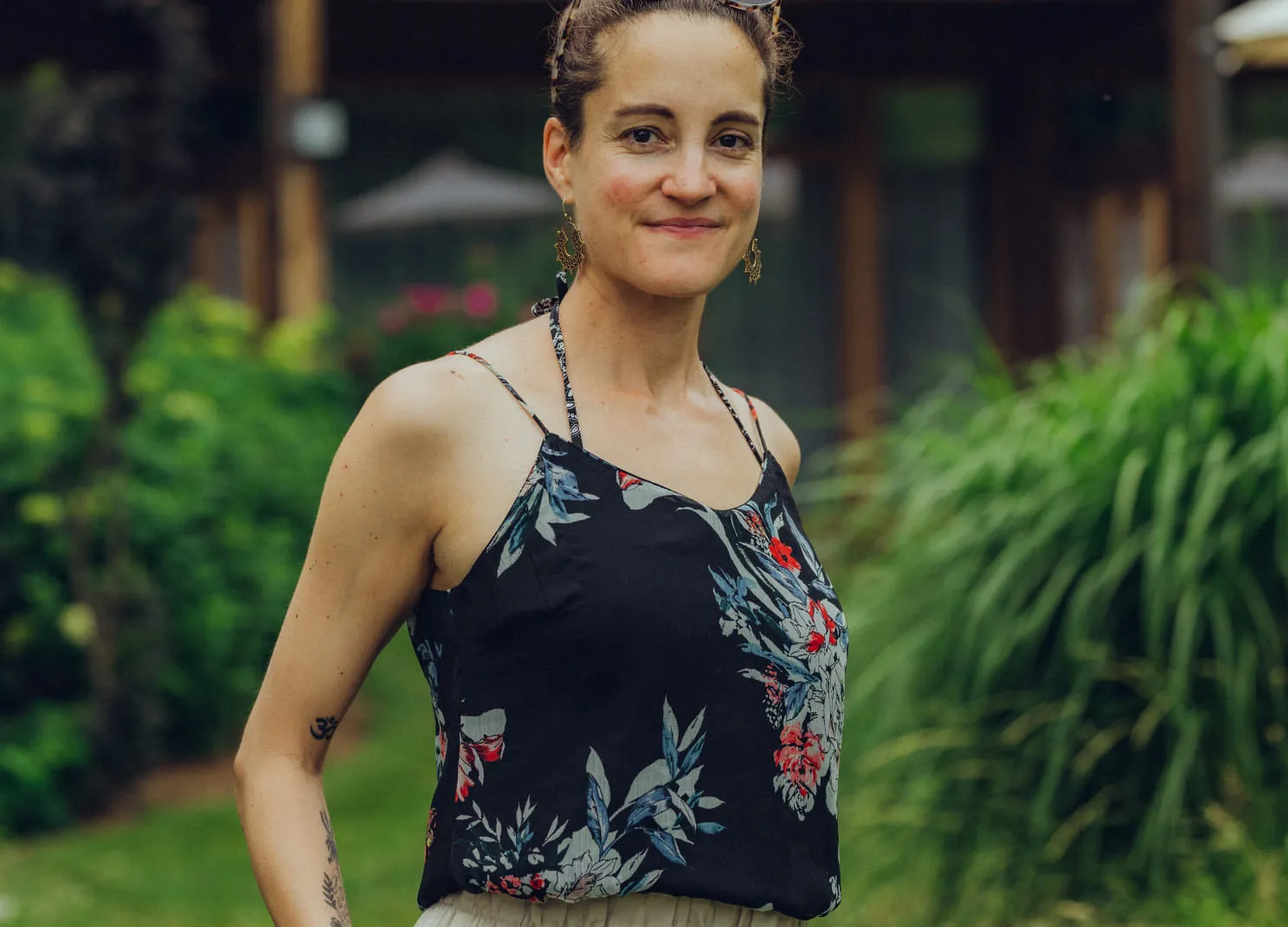 Frau im Garten, trägt ein Blumenoberteil, mit Pflanzen im Hintergrund