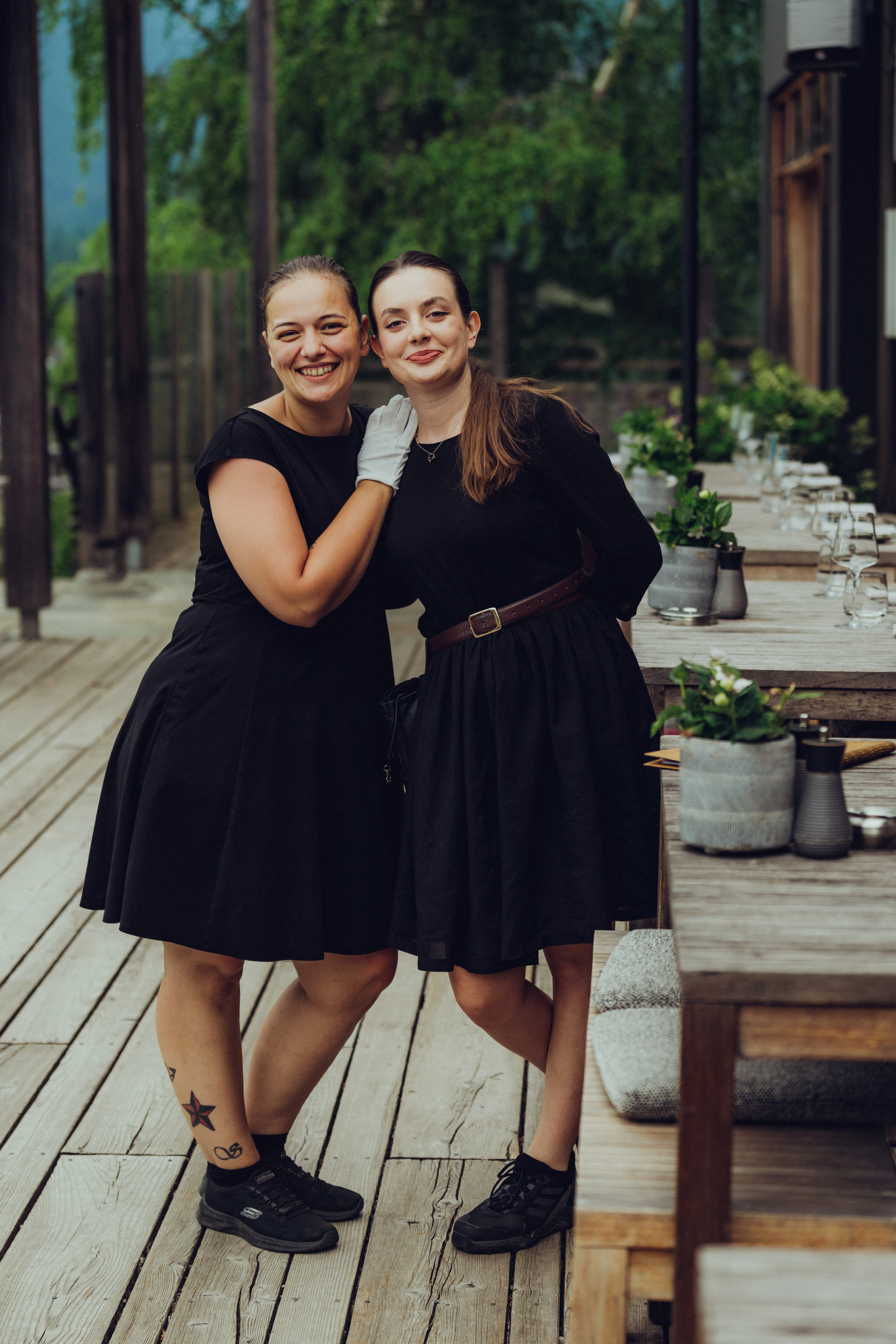 Zwei Frauen in schwarzen Kleidern auf einer Holzterrasse.