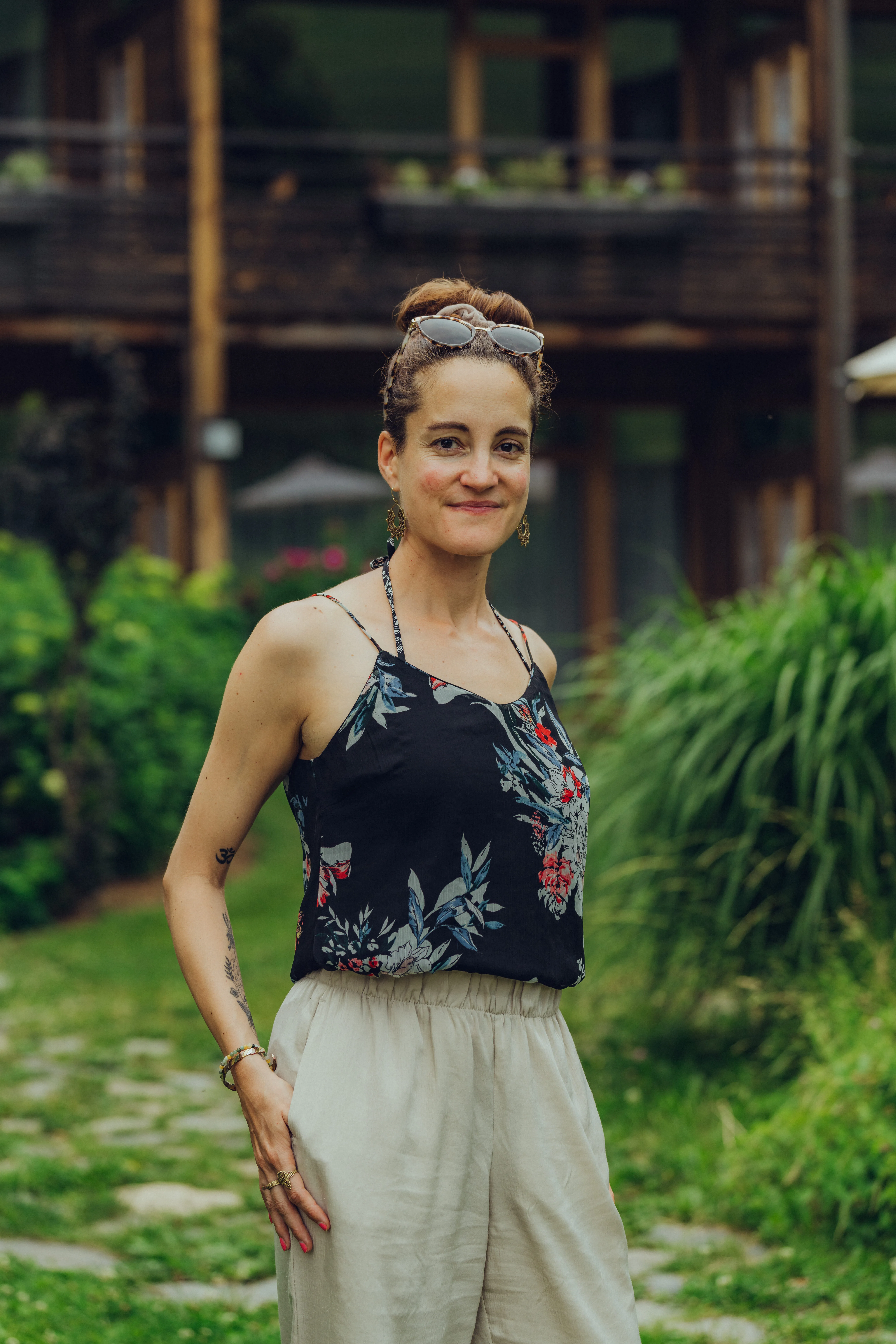 Frau in floralem Top und hellen Hosen, im Freien bei Pflanzen